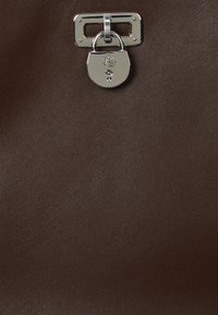 Brown leather handbag feature with silver hardware and a lock detail. The texture is smooth with a slight sheen.