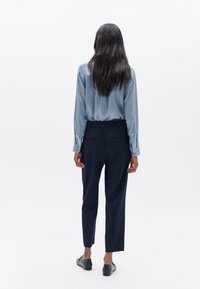 Blaue Satinbluse mit langen Ärmeln, kombiniert mit dunkelblauen, maßgeschneiderten Hosen. Glatte Texturen, tailliert, mit geradem Bein.