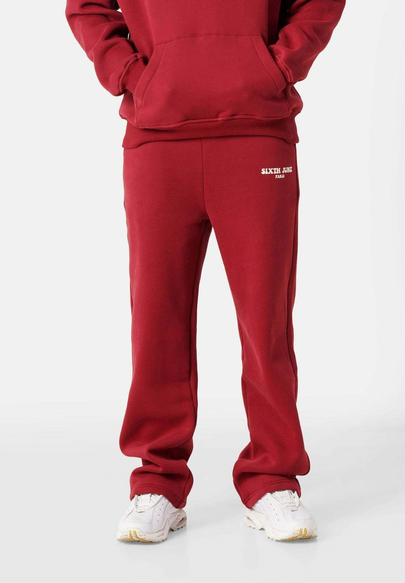 Rote Sweatpants aus weichem Stoff, mit einem weißen Logo am linken Oberschenkel, in entspannter Passform und mit elastischem Bund.
