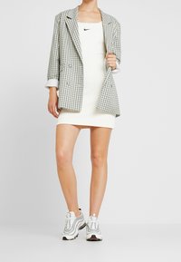 Blazer a quadri bianco e blu, abbinato a un vestito bianco a coste. In basso, sneakers bianche e metalliche con accenti neri.