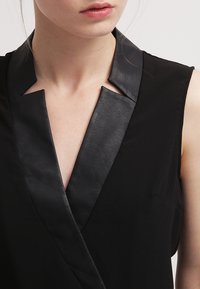 Czarny bezrękawnik z głębokim dekoldem w kształcie litery V, z kontrastującym kołnierzykiem przypominającym skórę oraz gładką teksturą materiału.