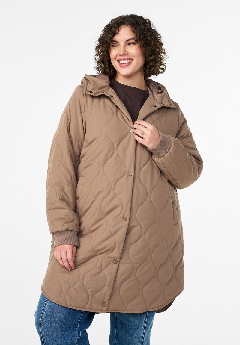 Tikkitakki, jossa on hupullinen pitkä ruskea takki, jossa on painonapit ja resorit hihansuissa. Kangas on sileää ja siinä on aaltoileva kuvio.