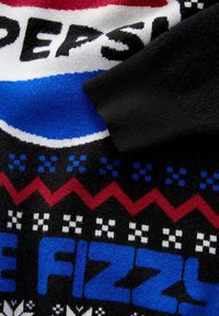Nahaufnahme eines gestrickten Stoffes, der einen Teil des Pepsi-Logos und den blauen Text "PIZZ" mit roten Zickzack- und karierten Mustern auf einem schwarz-weißen Hintergrund zeigt.