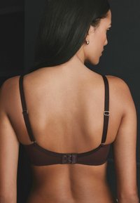 Brun bh med justerbare stropper, en hægte-og-øje lukning bagpå og en glat tekstur. Minimalistisk design uden synlige mønstre.