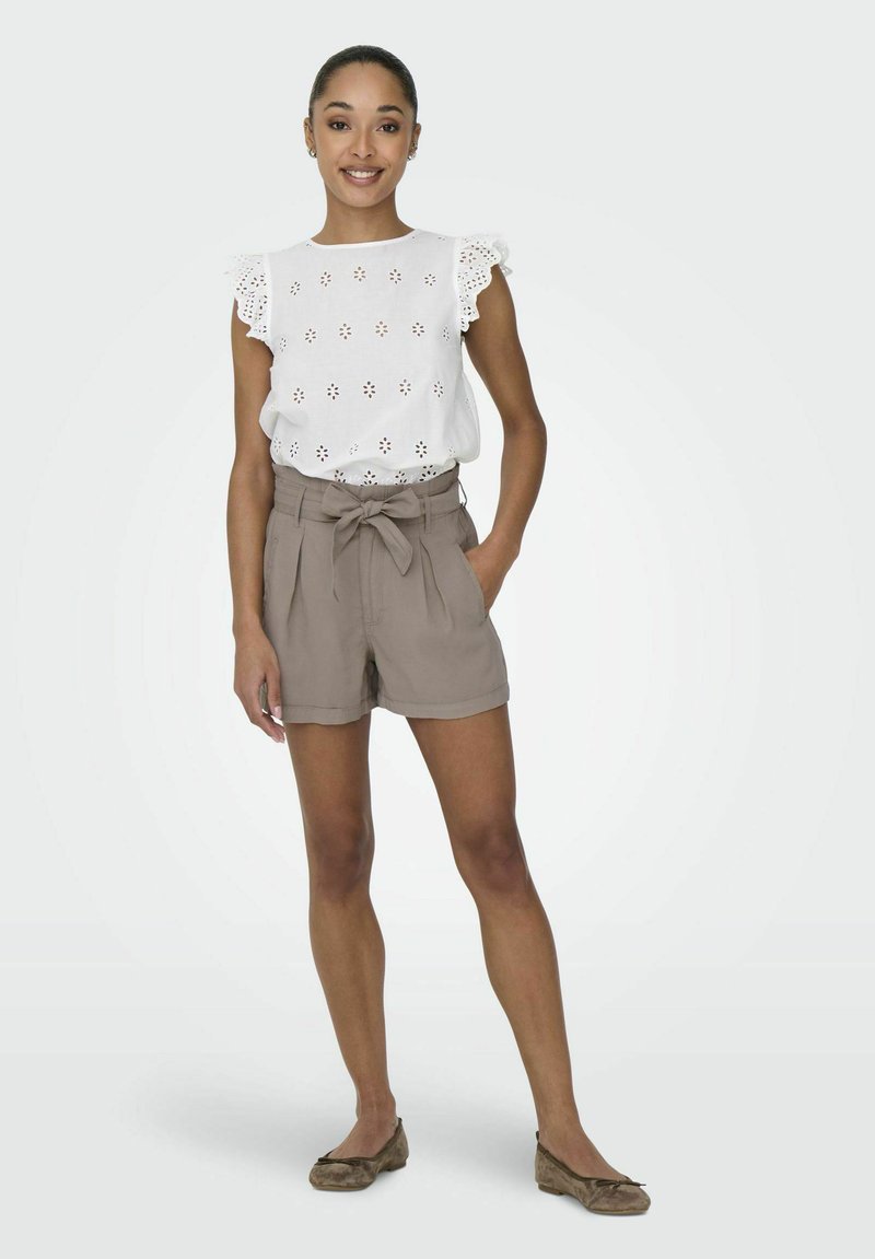 Witte blouse met oogjes en ruches aan de mouwen, gecombineerd met tan hoge taille shorts met een strik. Bruine ballerina's maken de outfit compleet.