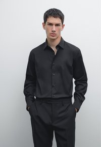 Black button-up shirt with long sleeves, collar, and front placket, paired with matching black trousers. Smooth fabric, fitted design.