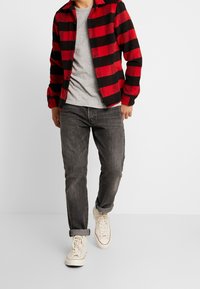 Rutig flanellskjorta i röd och svart över en grå T-shirt, i kombination med mörkgrå jeans och vita sneakers. Knapp-up design med uppkavlade ärmar.