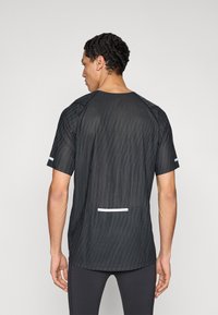 Musta urheilupaita, jossa on teksturoitu raidallinen kuvio, lyhyet hihat ja heijastavat valkoiset yksityiskohdat helmoissa ja hihoissa.