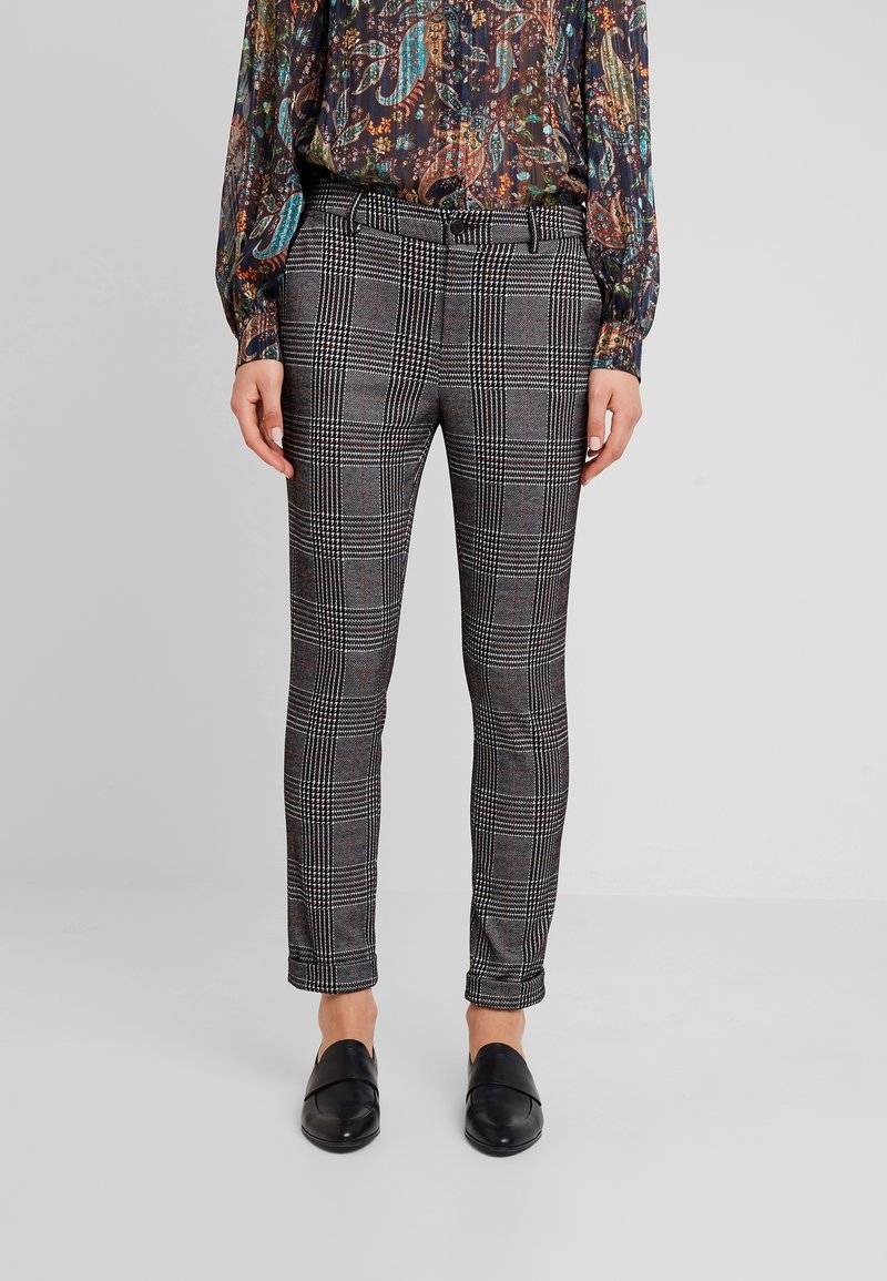 Pantalon à carreaux avec un motif noir, blanc et rouge, coupe slim, et un tissu lisse. Comprend une ceinture, avec des ourlets à la cheville et des mocassins noirs.