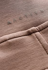 Brauner Sportbekleidungsstoff mit glatter Textur, ausgestattet mit einem auffälligen Logo "ACTIVE" in einer helleren Farbnuance und einfachen Nahtdetails.