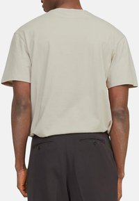 Beige T-Shirt mit kurzen Ärmeln aus weicher Baumwolle, klassischem Rundhals und legerer Passform, kombiniert mit dunklen Hosen.