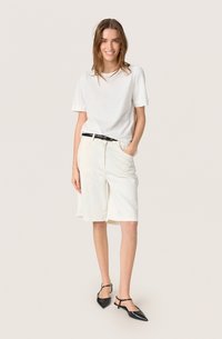 Witte t-shirt met korte mouwen en crèmekleurige knielange shorts, gecombineerd met zwarte slingback hakken. De outfit heeft een eenvoudig, casual ontwerp.