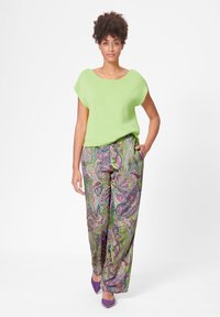 Limoengroene top met korte mouwen en een ronde hals, gecombineerd met gestreepte wijde broek met paarse, groene en roze paisley patronen.
