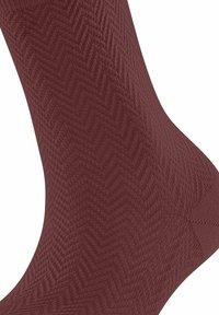 Chaussette bordeaux avec un motif chevron texturé, fabriquée dans un matériau doux avec une finition lisse, s'amincissant au niveau de la cheville.