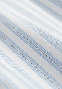 Katoenen stof met afwisselend witte en lichtblauwe strepen, voorzien van een subtiele structuur in de weving. Dunne donkere lijnen scheiden de strepen van elkaar.