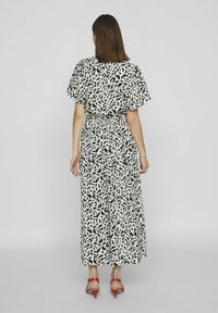 Vestito maxi bianco e nero a pattern con maniche corte, vita cintrata e gonna fluida. Indossato con sandali alti rossi.
