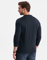 Man som bär en mörkblå långärmad tröja och blå jeans, sedd bakifrån, med kort brunt hår och armband på vänster handled.