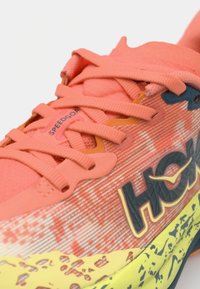 Coral and yellow running shoe featuring textured fabric, flat laces, and a logo on the side, with a rugged sole for traction.