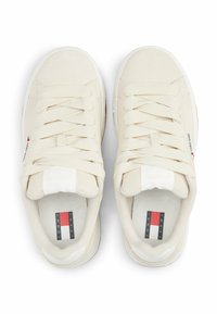 Baskets couleur crème avec une texture lisse, dotées de lacets plats, d'une languette rembourrée et d'une étiquette de logo avec des accents rouge, blanc et bleu.