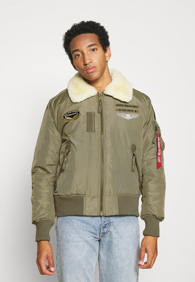 Olivgrüne Bomberjacke mit einem Kunstfellkragen, mehreren Patches, Reißverschlusstaschen an den Seiten sowie gerippten Bündchen und Saum.