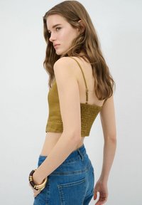 Olijfgroen crop top met dunne bandjes, textuur smocking aan de achterkant en een kantdetail aan de onderrand, gecombineerd met blauwe denim jeans.