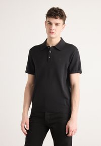 Čierna polo košeľa s krátkym rukávom vyrobená z pleteniny, s klasickým golierom, zapínaním na tri gombíky a diskrétnym logom značky na hrudi.