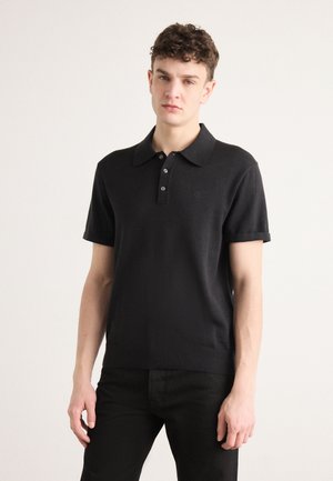 Svart kortärmad polo shirt i stickad tyg, med klassisk krage, treknapplås och subtil logotyp på bröstet.