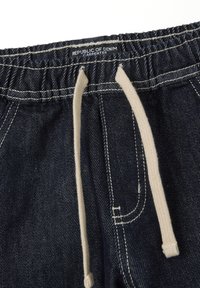 Pantalones de mezclilla azul oscuro con cinturilla elástica y cordones beige. Cuenta con costuras visibles, bolsillos y una etiqueta que dice "República del Denim."