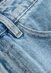 Ljust blå denimtextil med en synlig fick söm, kontrasterande orange överstygn och en mjuk, strukturerad yta.