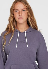 Paarse hoodie met witte trekkoorden, een voorknopzak en een geborduurd logo op de borst. Zachte, gestructureerde stof met een relaxte pasvorm.