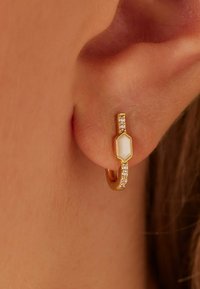 Gouden creolen hebben een geometrische witte stenen accent en een rij van kleine heldere edelstenen aan de voorkant.