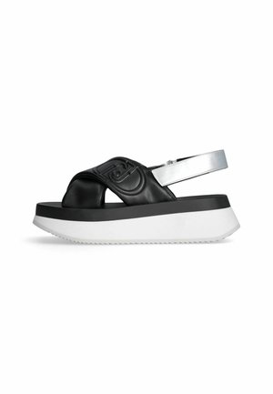 Sort og hvid platformsandal med tyk hvid sål, sorte polstrede krydsremme med præget design og sølv ankelrem med spænde.