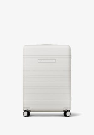 Hartschalenkoffer in mattem Weiß mit horizontalen Rillen, ausziehbarem Griff und vier schwarzen Rollen für Mobilität. Schlanker Kartensteckplatz auf der Vorderseite.