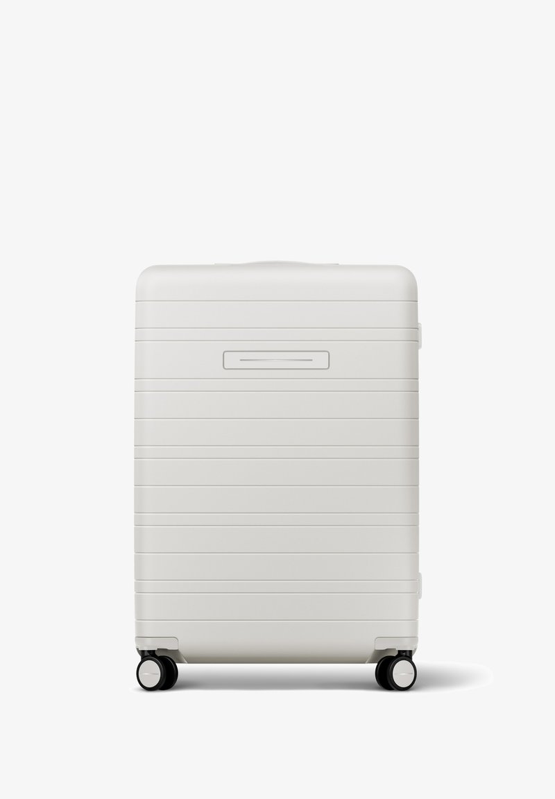 Hartschalenkoffer in mattem Weiß mit horizontalen Rillen, ausziehbarem Griff und vier schwarzen Rollen für Mobilität. Schlanker Kartensteckplatz auf der Vorderseite.