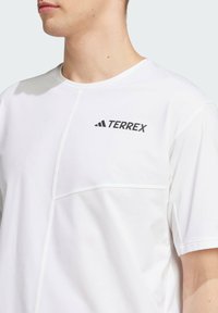 Hvid kortærmet T-shirt med rund halsudskæring, der har et sort "TERREX" logo og kontrasterende syninger på stoffet.