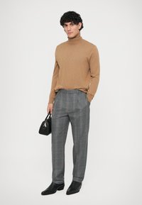 Pull à col roulé marron, pantalon à carreaux gris avec des accents orange, sac à main noir et chaussures en cuir noir. Coupe moderne, tissu texturé.