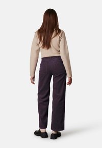 Fluwelen broek in donkerg paars met een wijd pijpenontwerp, gedragen met een beige trui. De outfit heeft achterzakken en een comfortabele pasvorm.