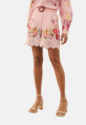 Ružové kvetované šortky s čipkovým lemom, k tomu zodpovedajúca ružová kvetovaná blúzka a béžové sandále na vysokom podpätku s remienkami okolo členkov.