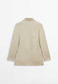 Blazer beige en tissu texturé, avec un col cranté, des manches longues et une fente centrale au dos pour faciliter les mouvements.