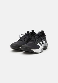 Des chaussures de sport noires avec un dessus en mesh texturé, des accents blancs contrastants, des lacets plats et une semelle en caoutchouc robuste. Design moderne avec une silhouette épurée.