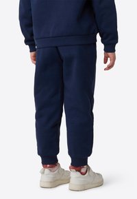 Mørkeblå joggebukser med elastiske mansjetter, laget av mykt materiale, kombinert med hvite joggesko. Designet har en minimalistisk stil.