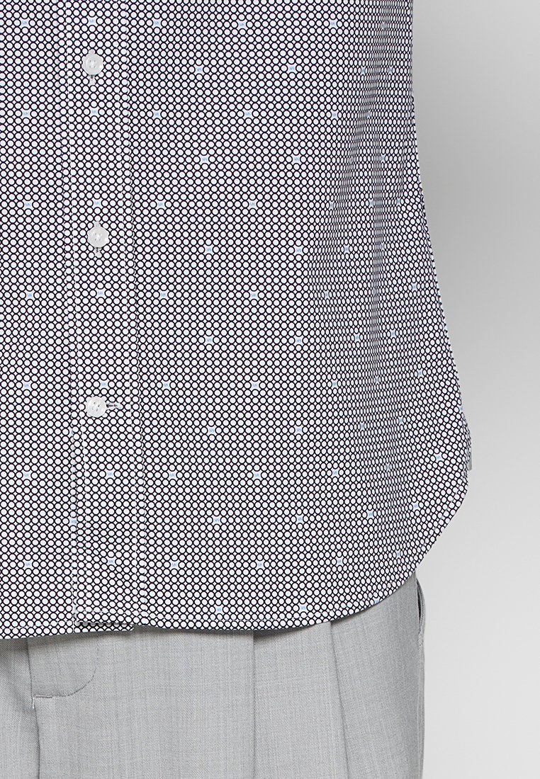Camisa abotonada con patrón hexagonal en blanco y negro, metida dentro de pantalones gris claro.