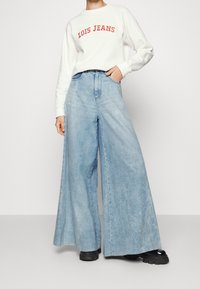 Jeans a gamba larga blu chiaro in denim, con vita alta e classico design a cinque tasche. Abbinati a un maglione bianco a collo rotondo.