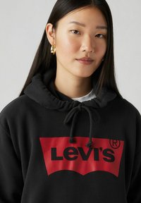 Sudadera negra con capucha y un logo rojo que presenta "Levi's" en letras negritas negras, capucha con cordón y detalles de puños elásticos.