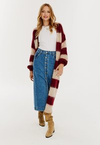Dlhý pruhovaný kardigán v červenej a krémovej farbe, skombinovaný s bielym topom a vysoko pásovými modrými džínsovými sukňami s gombíkovým zapínaním. Béžové čižmy po kolená.
