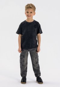 Svart t-shirt med kort ärm och subtil logotyp, i kombination med grå cargobyxor med sidofickor och elastiska muddar, bärs tillsammans med svarta sneakers.