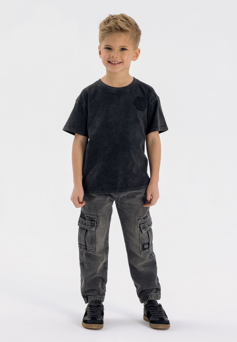 Svart t-shirt med kort ärm och subtil logotyp, i kombination med grå cargobyxor med sidofickor och elastiska muddar, bärs tillsammans med svarta sneakers.