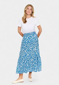 Fustă maxi florală albastră cu tiv cu volane în straturi și talie elastică, asortată cu un tricou alb simplu și balerini de culoare deschisă.