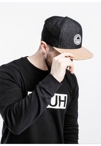 Black denim cap with a cork brim, featuring a circular logo patch. Black sweatshirt with white text "HUH" displayed on the front.