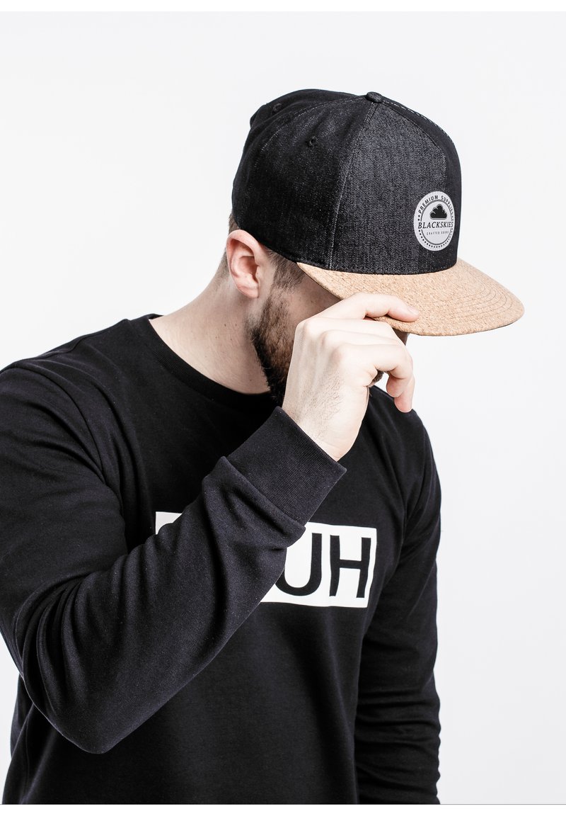 Black denim cap with a cork brim, featuring a circular logo patch. Black sweatshirt with white text "HUH" displayed on the front.